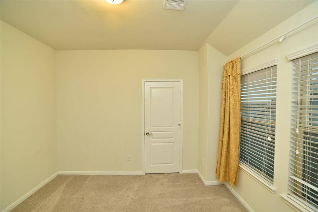 2nd Bedroom (11'6x10').This room features neutral walls and carpeting, a white door, and large windows with blinds and gold curtains, allowing for ample natural light.