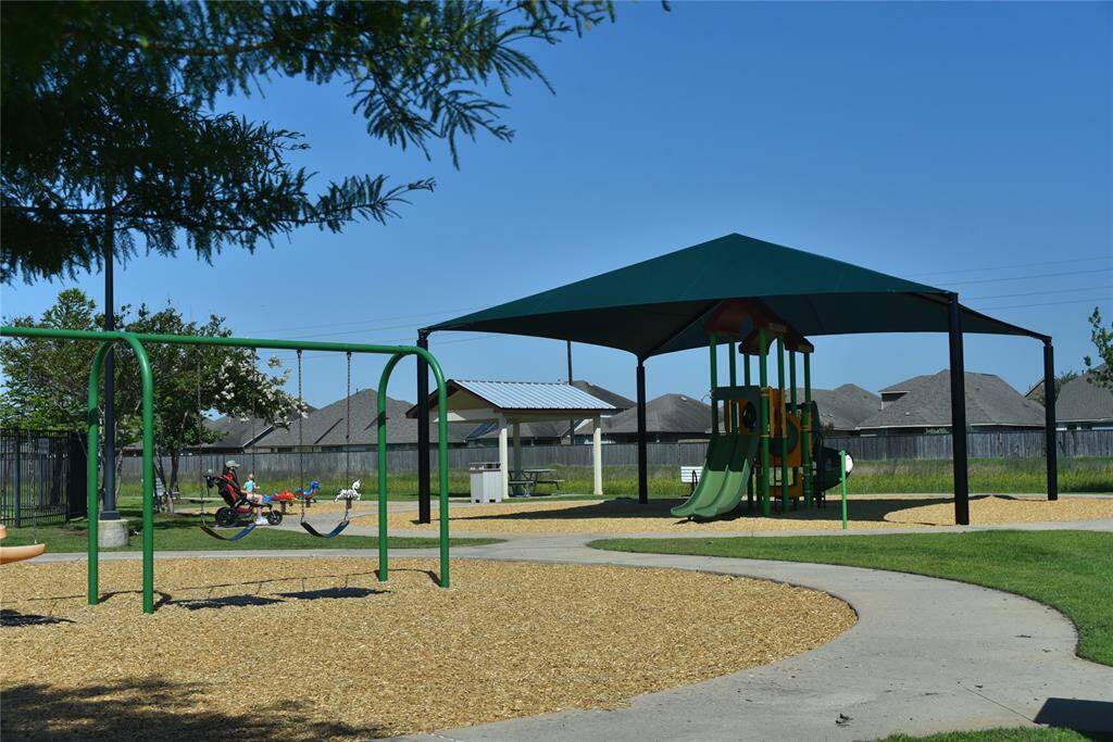 A well-maintained community playground featuring swings, a covered slide structure, and picnic area, set in a peaceful neighborhood environment.