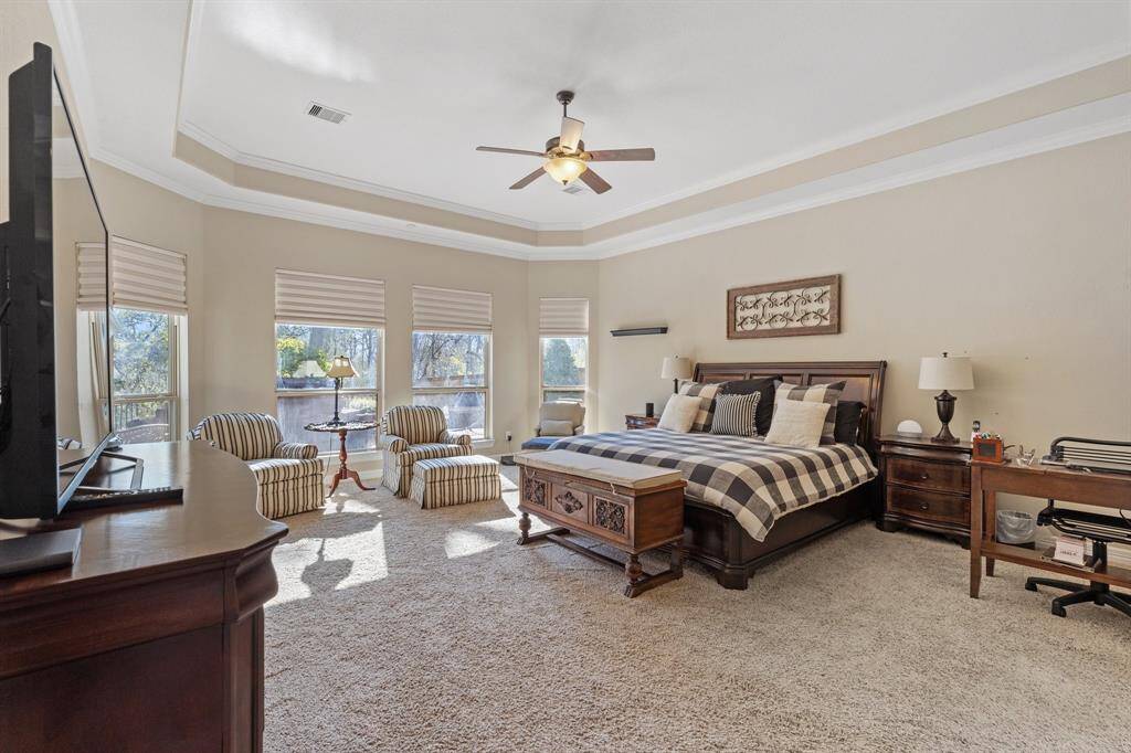 Primary bedroom suite featuring a bay window with a view of the pool, crown molding, and tray ceilings, creating a luxurious and relaxing retreat.