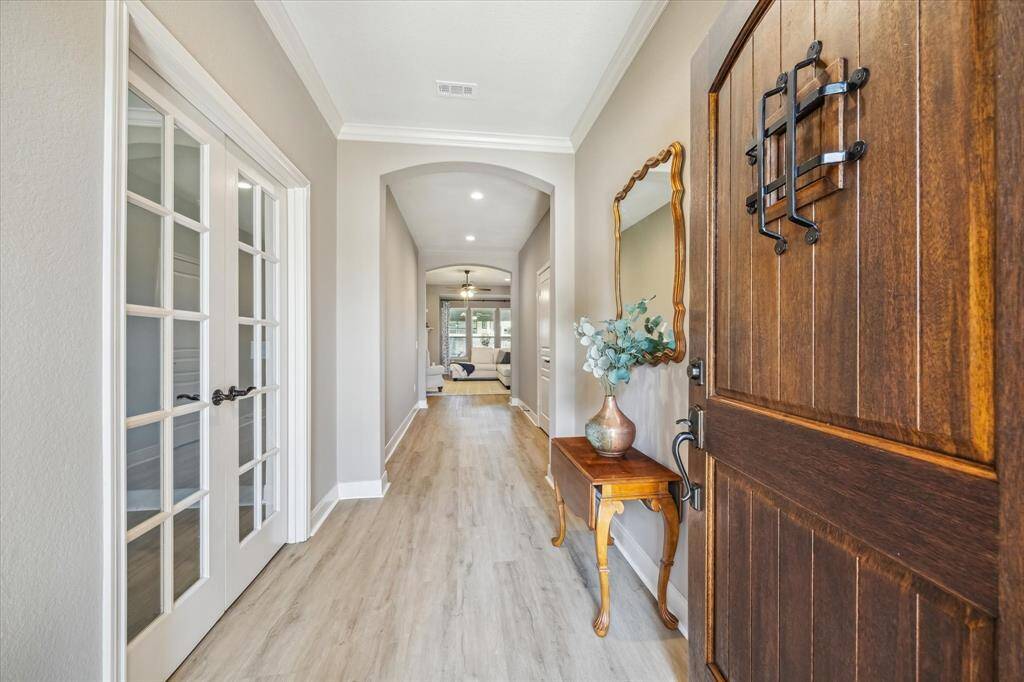 Welcoming entryway with a wooden front door, light luxury vinyl plank flooring, and elegant French doors leading to the home office. This entryway leads you down the hallway to a cozy living area.