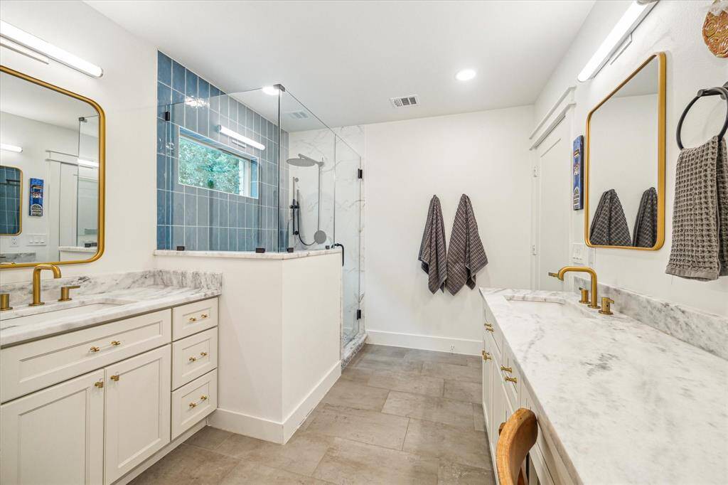 Modern primary bath with bright lighting, glass shower, dual sinks, and stylish base cabinets.