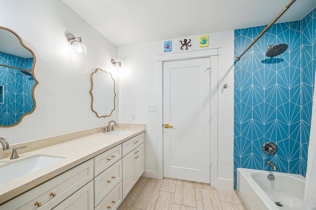 Clean, bright bath offering a tub/shower combo, dual sinks, sconces, and base cabinets.