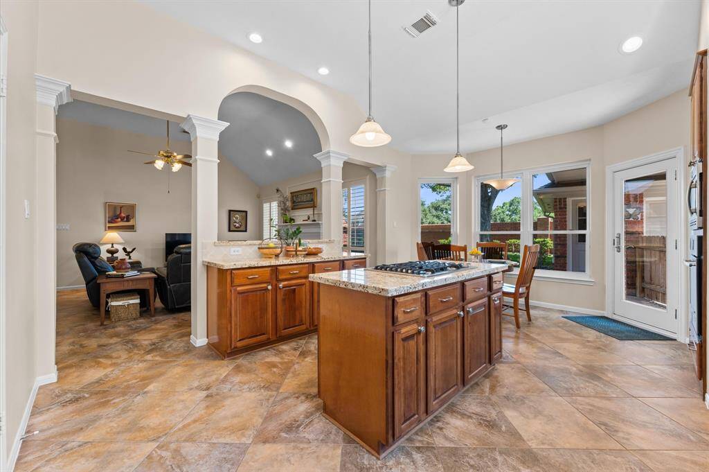The kitchen has cherry cabinets, granite countertops, and pendant lighting over the island with gas cooktop. Columns with double crown molding and an arched opening to the family room bring elegance to the kitchen.