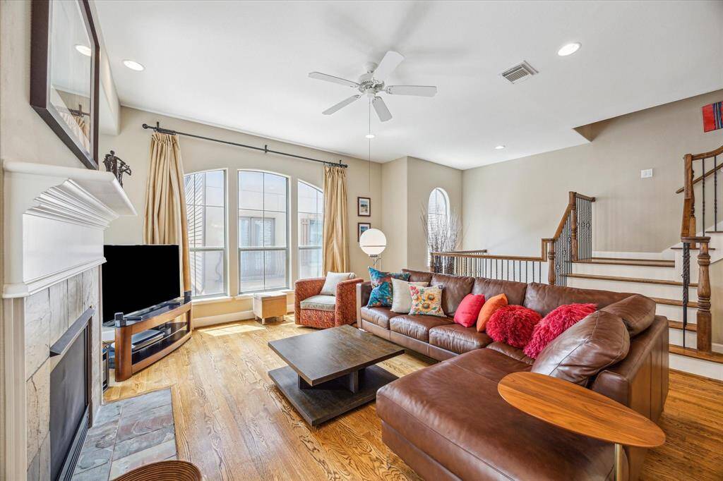 Large arched windows and tiered ceiling heights draw natural light into the second-floor living area, where a stone-framed fireplace and elegant iron stair railing create a polished yet comfortable backdrop for daily living or entertaining.