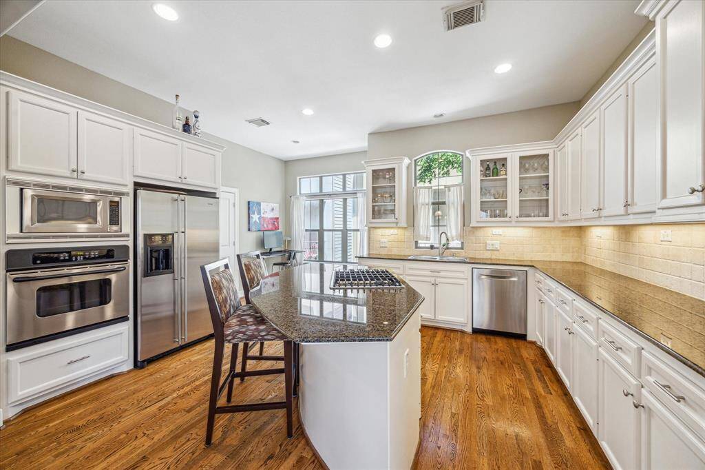 Granite countertops, stainless appliances, and custom cabinetry line this bright and spacious kitchen, anchored by a central island with a gas cooktop and bar seating, ideal for casual meals or entertaining.