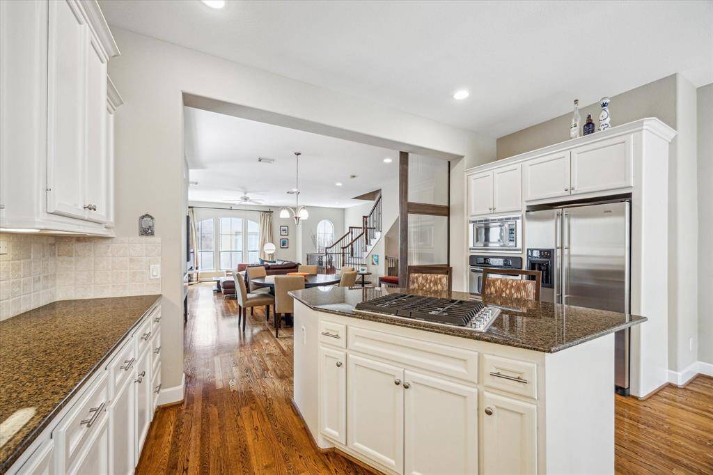 The kitchen’s large island with gas cooktop and bar seating anchors the space, surrounded by stainless appliances, double ovens, and extensive cabinetry that extends into the open living and dining areas for effortless flow.