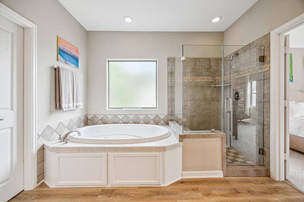 Jetted soaking tub sits beside a frameless glass shower, surrounded by neutral tile and soft natural light. Clean lines and classic finishes create a timeless feel in this spacious ensuite.