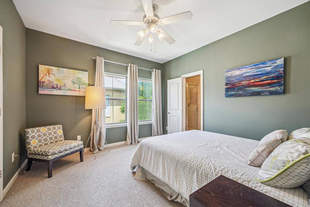 Rich green accent walls add depth and warmth, while tall windows with soft drapes fill the room with natural light. Neutral carpet flooring complements the space, and elevated ceilings enhance the sense of openness. Private en suite bath access and thoughtful layout make this secondary bedroom feel both stylish and secluded.