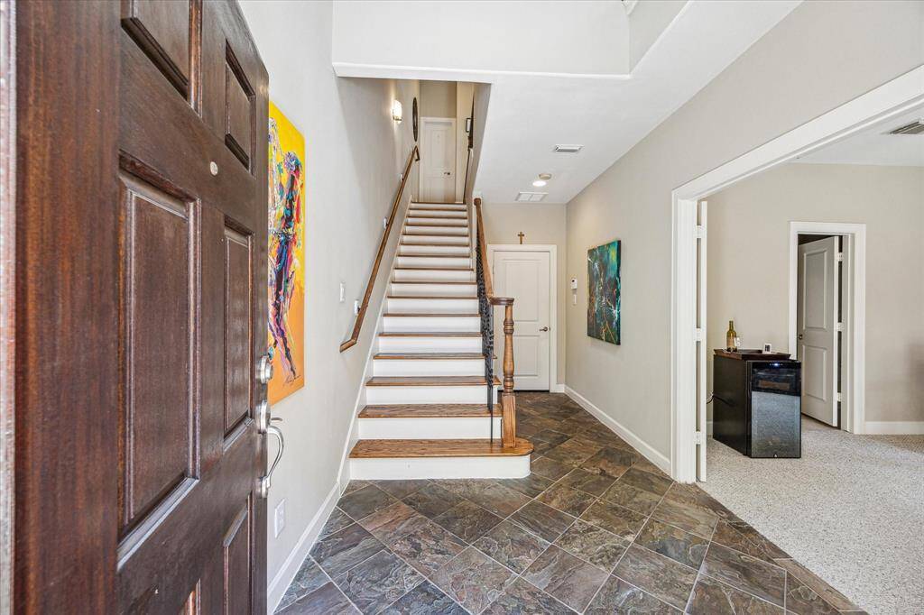 Step inside to a light-filled entry with slate tile flooring, high ceilings, and a wide staircase accented by wood treads and a wrought iron banister. The layout offers a warm, functional flow, with direct access to a first-floor bedroom or office just off the foyer.