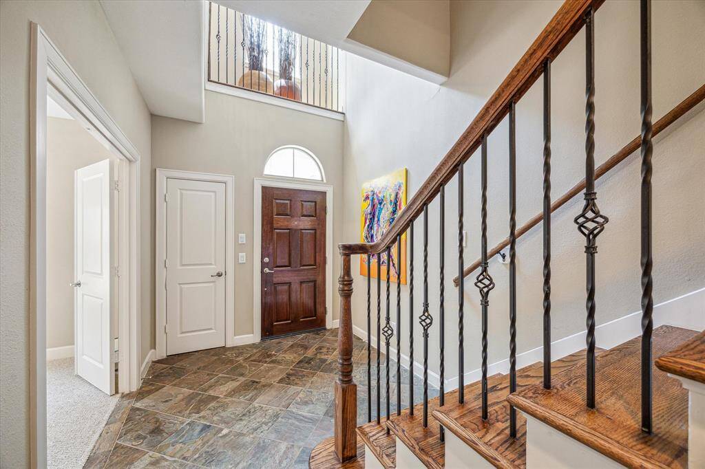 Natural light pours through the arched transom window above the front door, highlighting the slate tile floors and soaring ceiling. A warm wood staircase with decorative iron balusters adds elegance while drawing the eye upward to the second-floor landing.