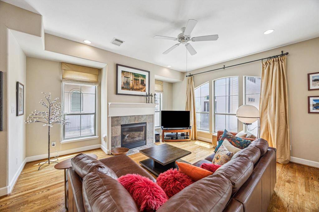 Anchored by a stone fireplace and surrounded by tall arched windows, the living room offers a bright and inviting space to relax or gather, with hardwood floors adding warmth and flow throughout the second-floor layout.