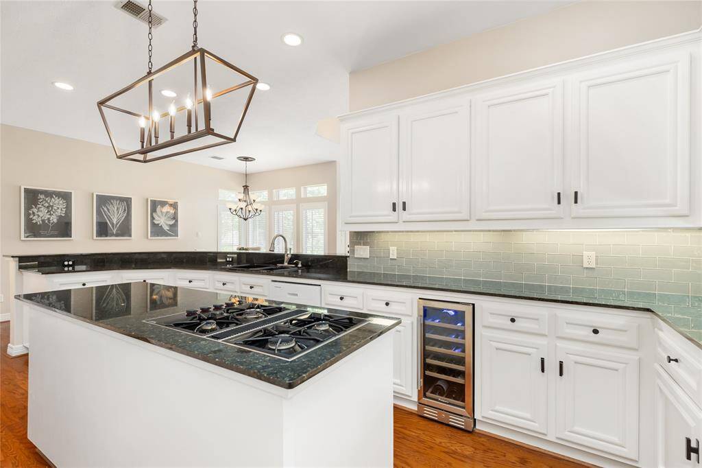 Updates include the built-in wine cooler, undercabinet lighting, recently added glass tile backsplash, black quartz counters, and lighting.