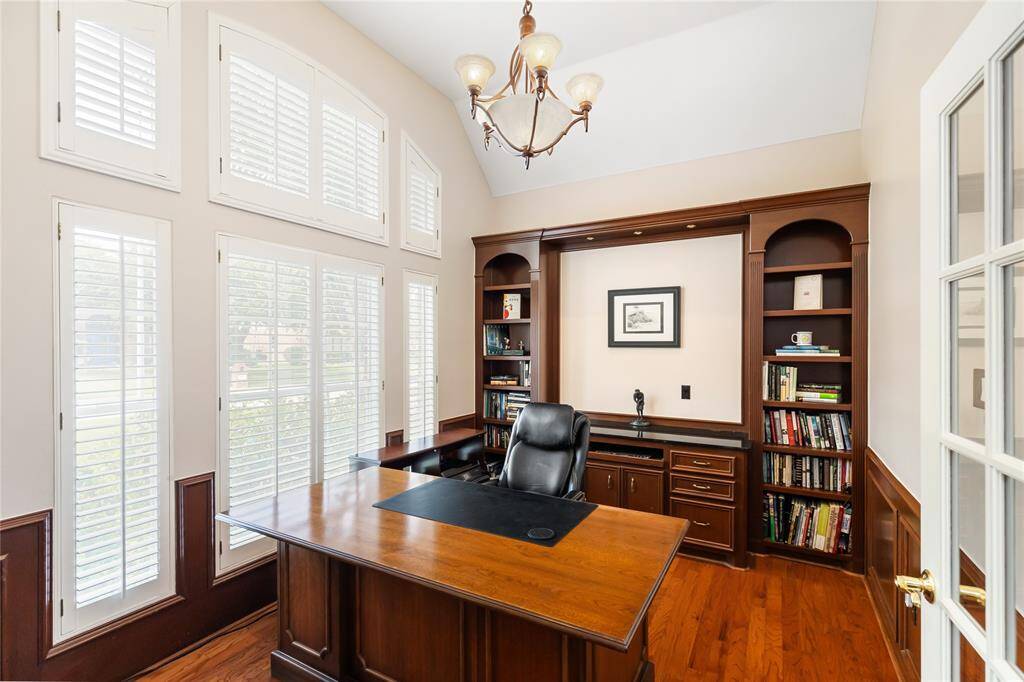 French doors lead into the private Office, which features a built-in desk, credenza, and bookcases that match the wood paneled walls, plus arched windows which overlook the front yard through plantation shutters.