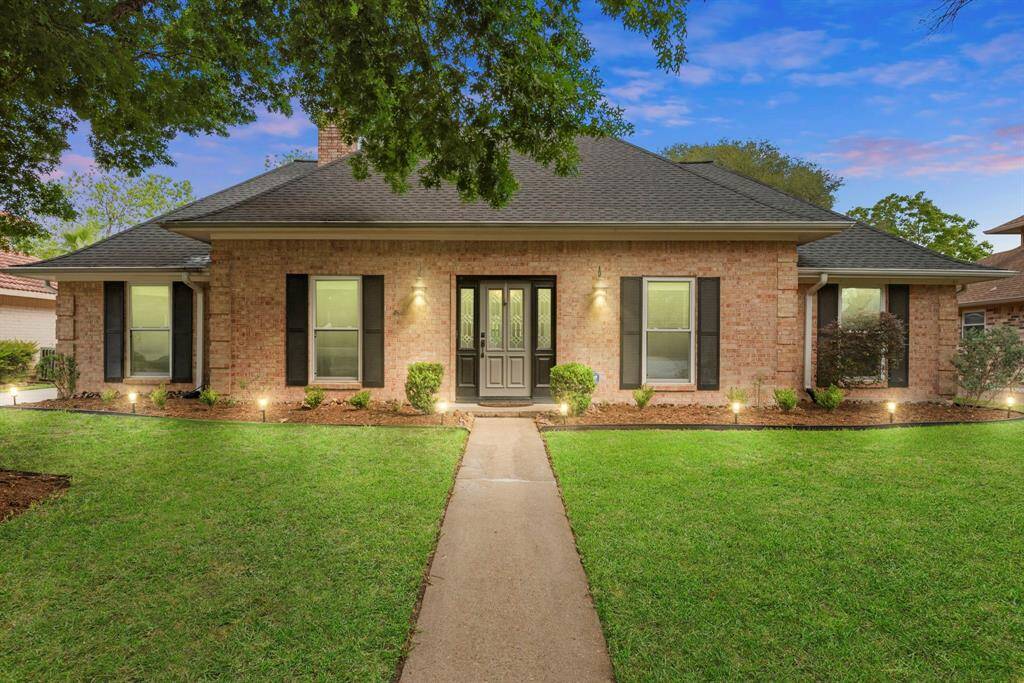 This inviting home features a classic brick exterior with a well-maintained lawn and a charming walkway leading to the front door. It has a symmetrical design with large windows and mature landscaping, offering great curb appeal.