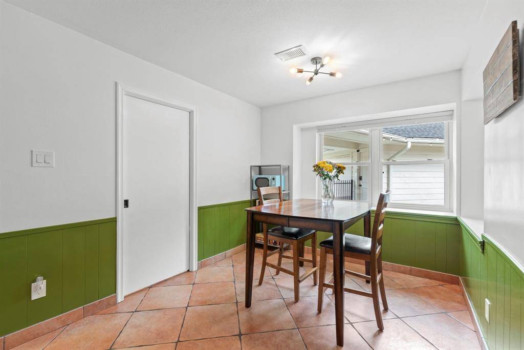 This cozy breakfast area features a modern light fixture, wrap around windows providing plenty of natural light.The space is accented with green wainscoting and terracotta tile flooring, creating a warm and inviting atmosphere.