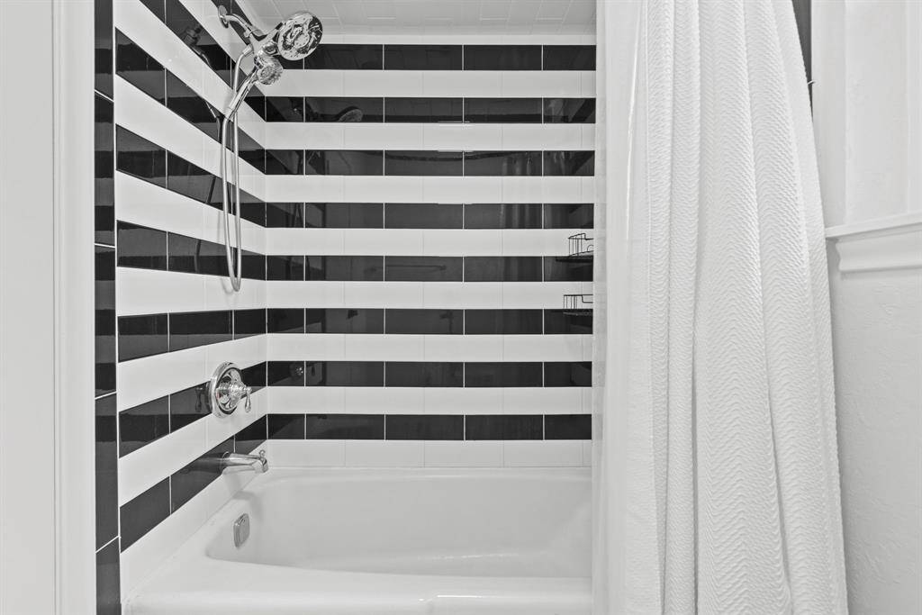 This bathroom features a modern tub and shower with a black and white striped tile design, complemented by a sleek, handheld shower head.