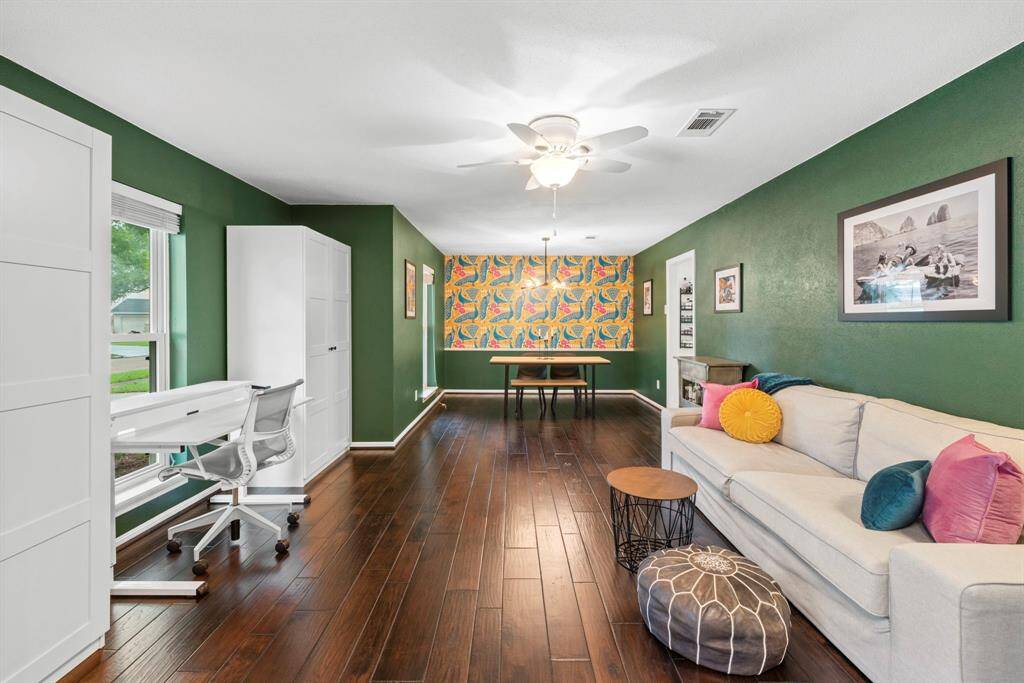This vibrant formal living and formal dining space features rich hardwood floors and deep green walls. Large windows offer ample natural light, creating a warm and inviting atmosphere.