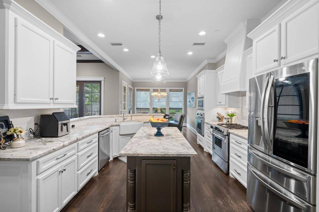 This kitchen features elegant white cabinetry, stainless steel appliances, honed dolemite counters, and a spacious island.