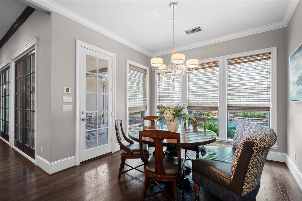 This cozy breakfast area with large windows allowing natural light and garden views. The space is accented by a modern chandelier, wood flooring, and glass-paneled doors leading to the covered patio.