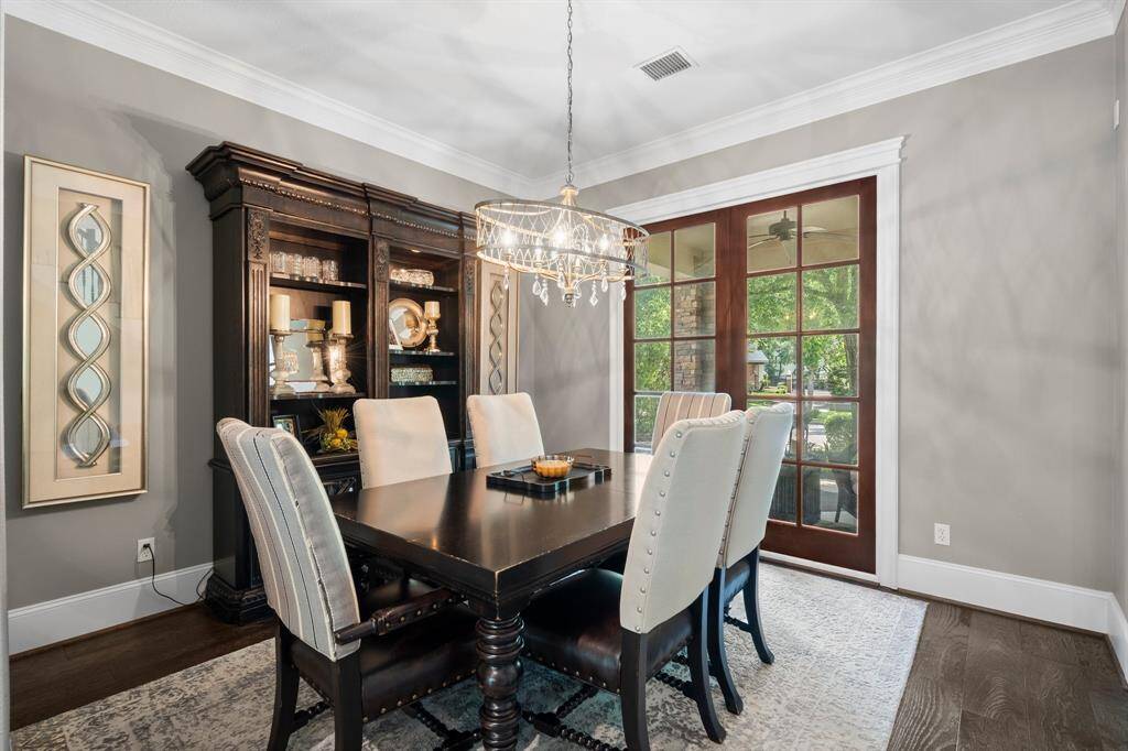The elegant formal dining room features neutral walls and a stylish chandelier. French doors lead to a lush outdoor view.