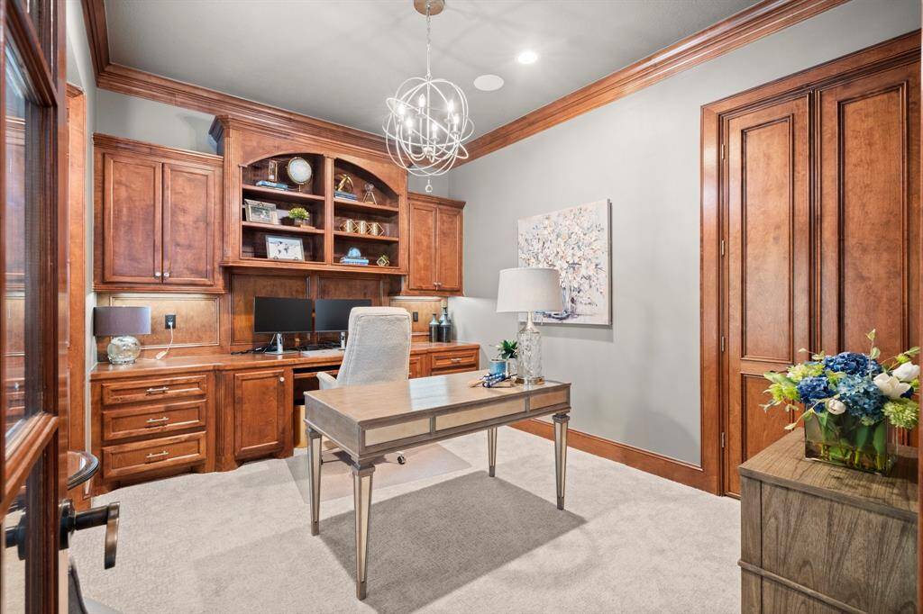 Home office with elegant wooden cabinetry and comfortable lighting. The room features soft carpeting and built-in shelves, creating a warm and inviting workspace.