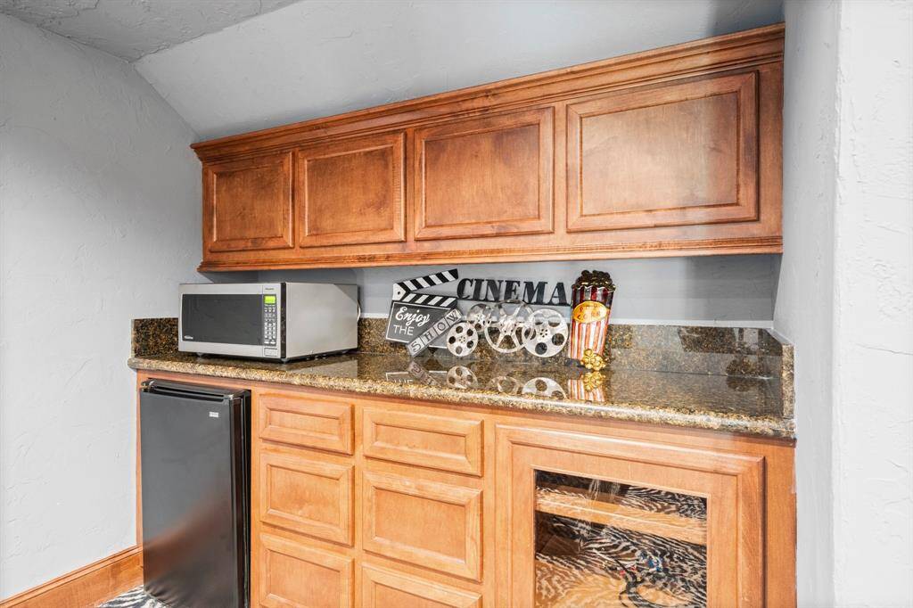 Home theater kitchenette features granite countertops, a microwave, and a mini fridge, perfect for movie night snacks and drinks.