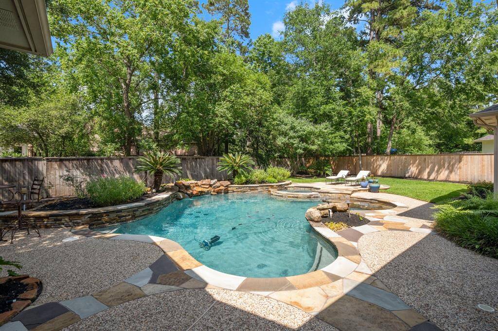 This inviting backyard features a beautifully designed pool with a stone surround and adjacent hot tub. Lush greenery and mature trees provide privacy, while a spacious patio area offers ample space for relaxing or entertaining. Perfect for enjoying sunny days in a serene setting.
