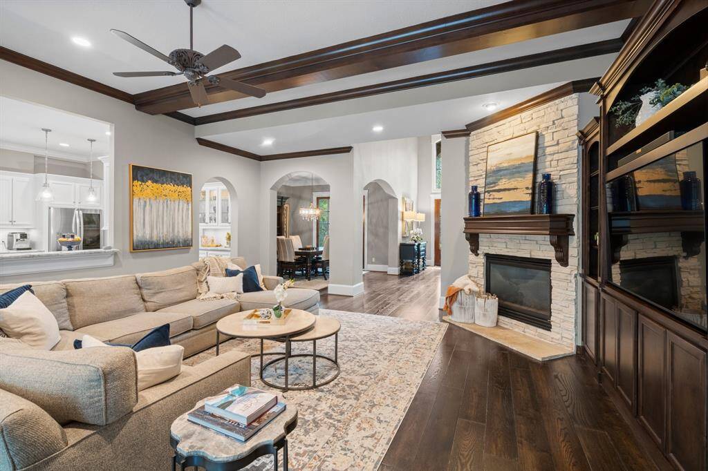 Stone fireplace and elegant wooden beams. The open layout flows into a modern kitchen, while decorative arches lead to a dining area.