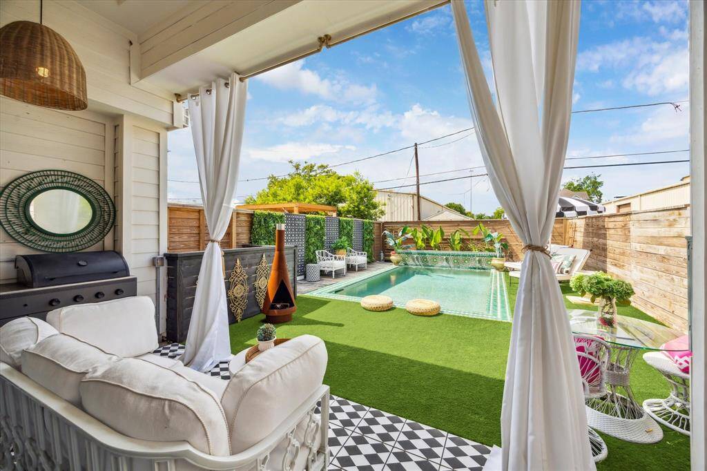 Stylish outdoor space with a cozy covered patio featuring a grill and seating. It opens up to a private pool area surrounded by artificial turf and decorative fencing, offering a serene and inviting atmosphere for relaxation and entertainment.