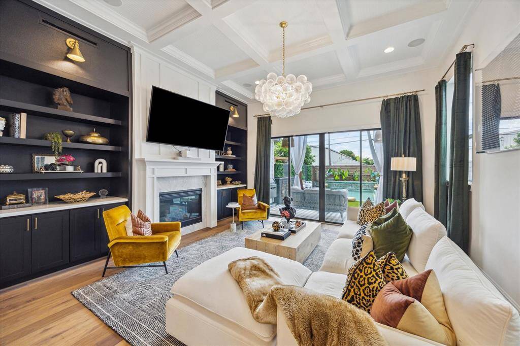 Inviting living room features a cozy fireplace, built-in shelving, and a large TV. It offers ample natural light through sliding glass doors, leading to backyard oasis. Elegant decor, a plush sectional, and stylish accent chairs create a comfortable atmosphere.