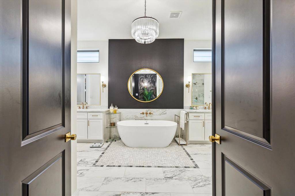 Luxurious bathroom features a freestanding bathtub and a striking black accent wall. It offers dual vanities with ample counter space and gorgeous flooring.