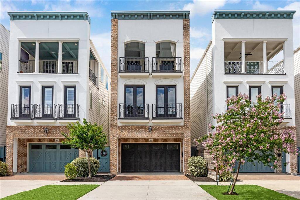 Three-story townhouse with a brick and stucco facade. The home has a spacious garage and is flanked by well-maintained trees, offering a blend of elegance and functionality in a contemporary design.