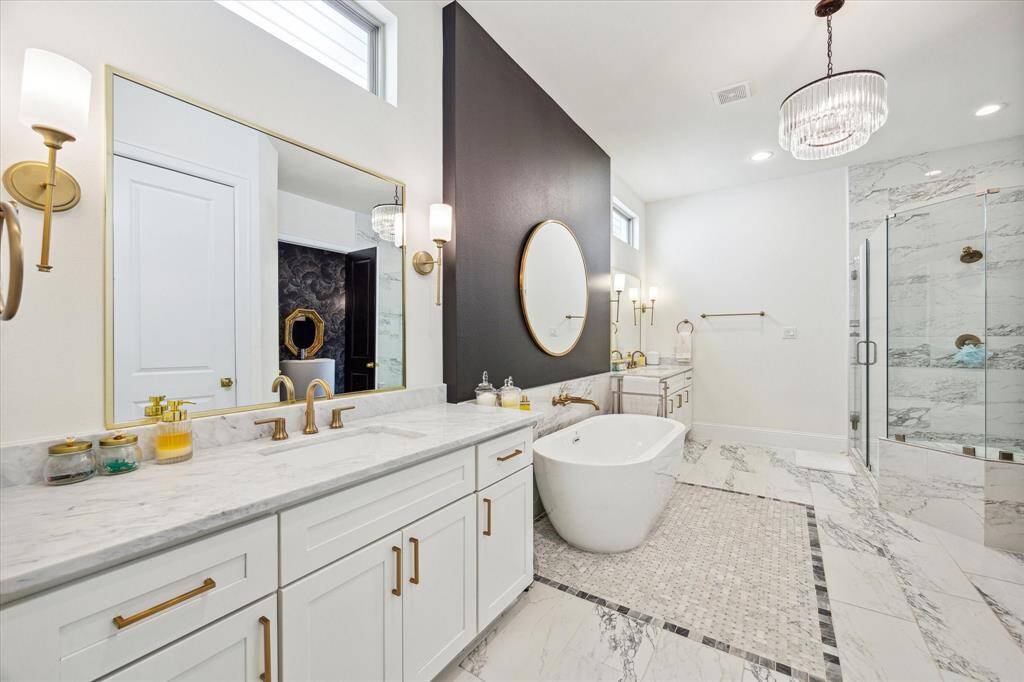 This luxurious bathroom features a modern design with a freestanding tub, dual sinks with marble countertops, a spacious glass-enclosed shower, and elegant lighting fixtures. The white and gray color scheme adds to the spa-like atmosphere.