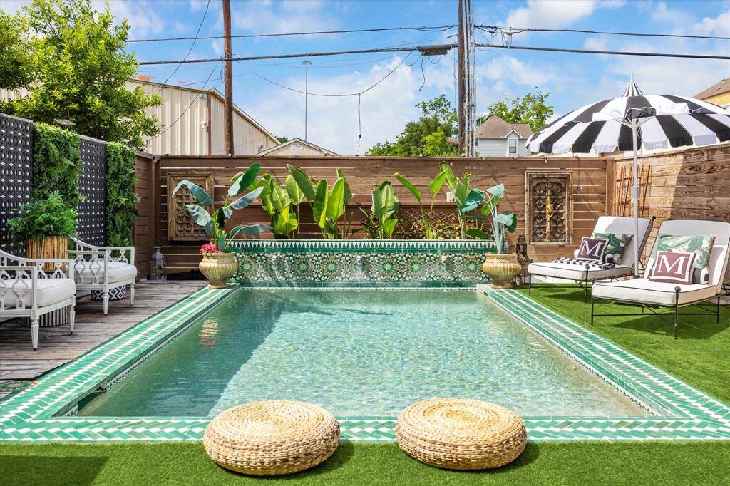 Charming backyard oasis featuring a stylish, tiled pool surrounded by lush greenery and chic seating. Perfect for relaxation and entertaining.