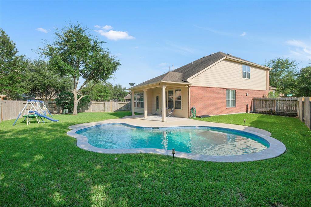 This backyard has everything you need to beat the heat; a refreshing pool, shade from mature trees, and a covered back patio.
