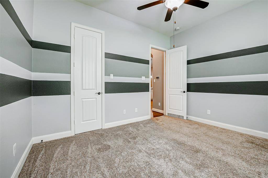 This room features modern striped walls in neutral tones, a plush carpet, and a ceiling fan.