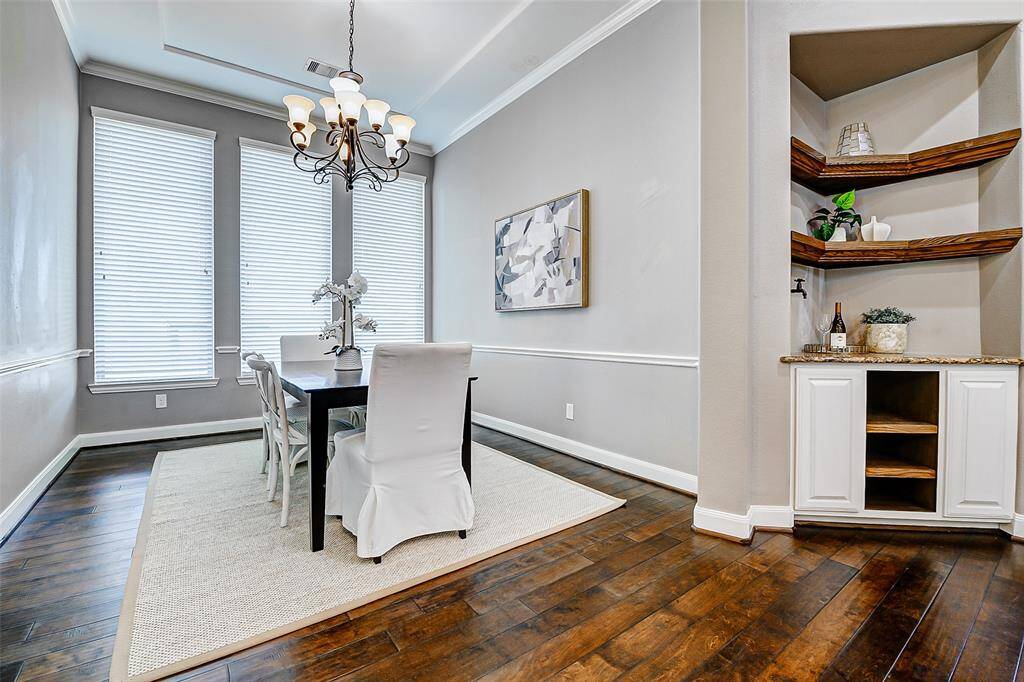 This photo showcases a bright dining room with elegant hardwood floors and large windows, allowing natural light to fill the space. It features a modern chandelier, and a stylish custom built-in corner coffee bar with water spout.