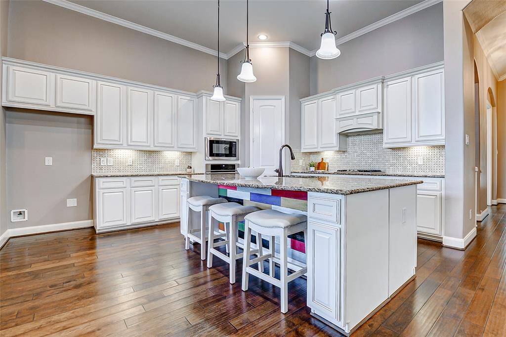 The  kitchen features elegant white cabinetry, granite countertops, and a large island with breakfast bar seating. The hardwood floors and modern pendant lighting add a touch of sophistication, while the stainless steel appliances and ample storage make it highly functional.
