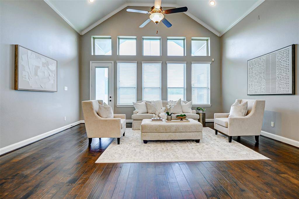 This photo showcases a spacious, well-lit living room with high ceilings and large windows. It features elegant hardwood floors, neutral-toned walls, and comfortable seating, creating a welcoming and stylish atmosphere.