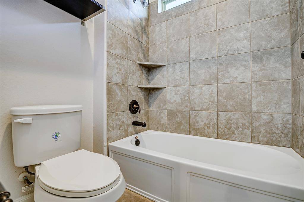 This bathroom features a modern design with a tiled shower and bathtub combo, built-in corner shelves, and a clean white toilet. The neutral tones create a welcoming and fresh atmosphere.
