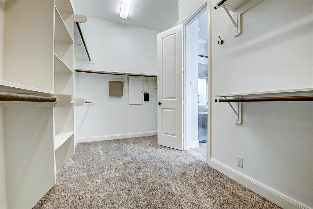 Spacious walk-in closet with carpeted flooring, ample shelving, and hanging rods. Brightly lit with an open door leading to an adjoining bathroom. Ideal for organization and storage.