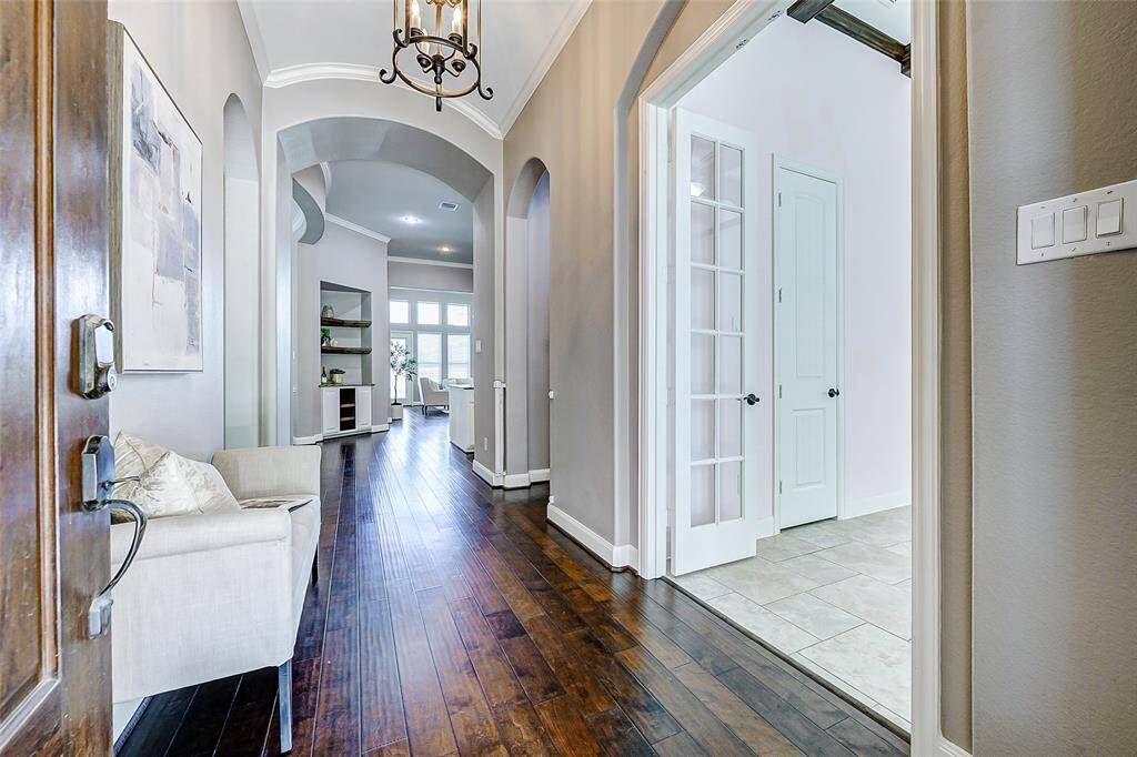 Inviting entrance with a warm, hardwood floor leading to a bright living area. Features high ceilings, elegant archways, and a modern light fixture, creating an open and welcoming atmosphere.