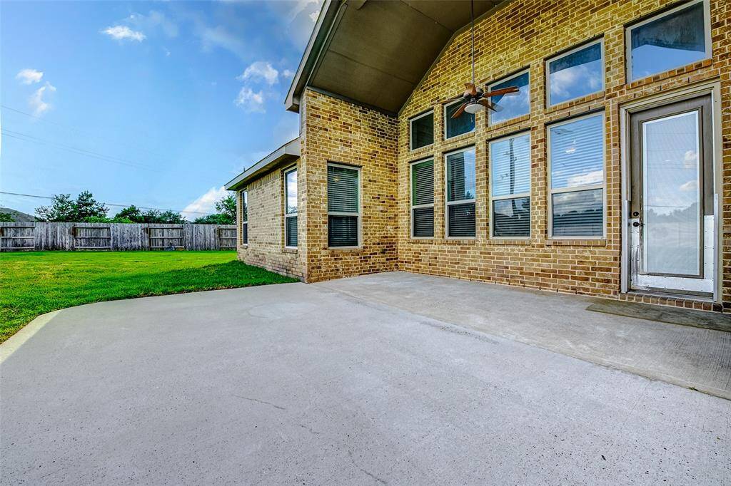 This photo showcases a spacious, covered patio with a ceiling fan, ideal for outdoor gatherings. It features a brick exterior with large windows, providing plenty of natural light. The patio overlooks a well-maintained, fenced backyard, perfect for relaxation and privacy.
