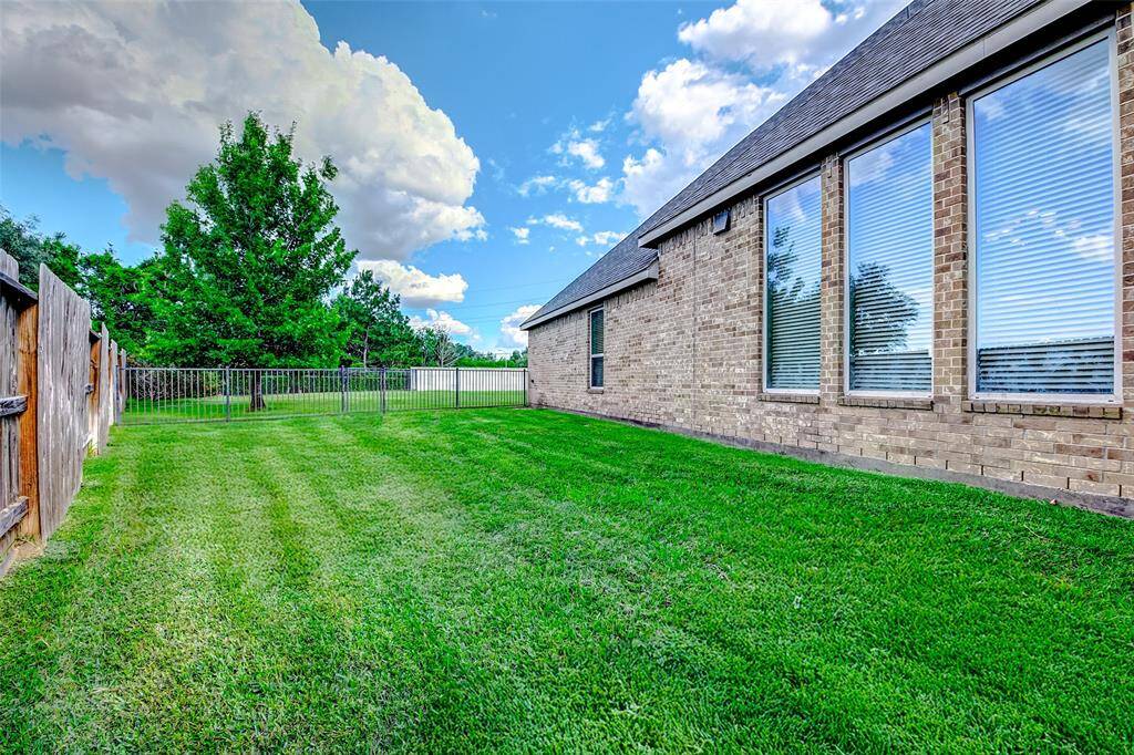 This photo showcases a well-maintained backyard with lush green grass, a brick exterior, large windows, and a wooden fence, offering privacy and a serene setting.