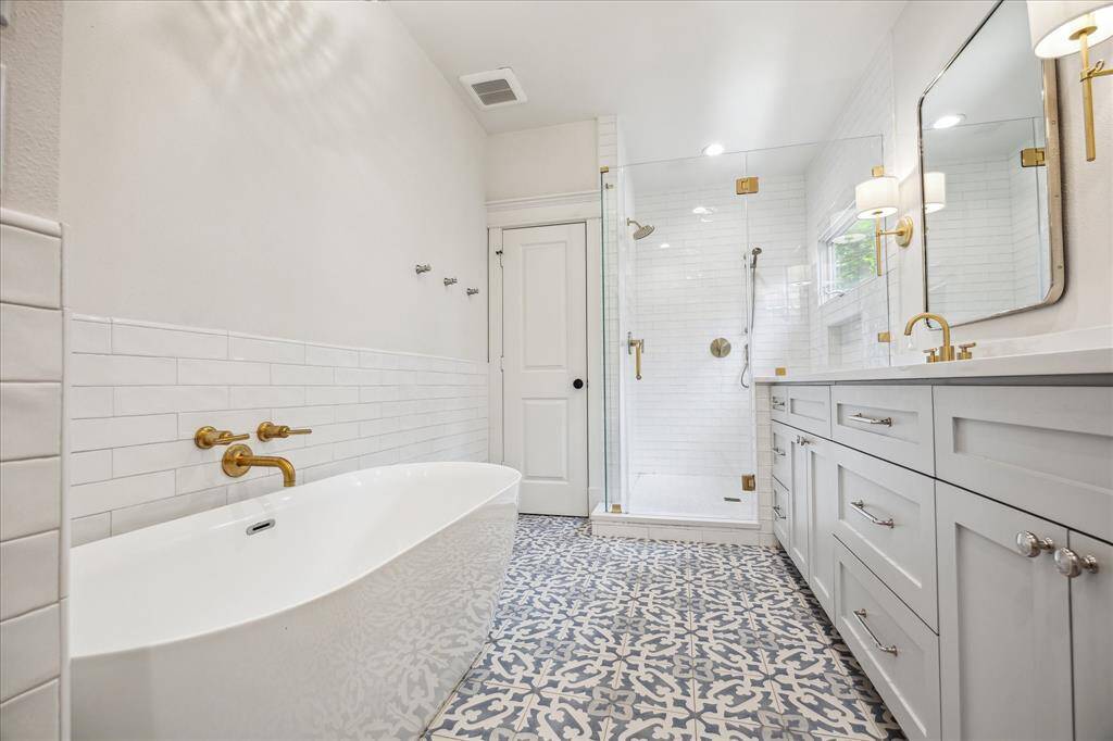 Fully renovated primary bathroom that features tile floor, a large vanity with two sinks with beautiful wood cabinetry. Also features a walk-in shower with tile surround and frameless door.  Separate free standing soaking tub and private water closet.
