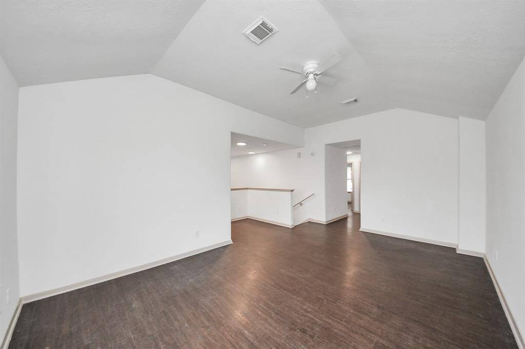 This spacious room features high ceilings, a ceiling fan, and dark wood flooring. It's bright with neutral walls, offering a modern, open feel.