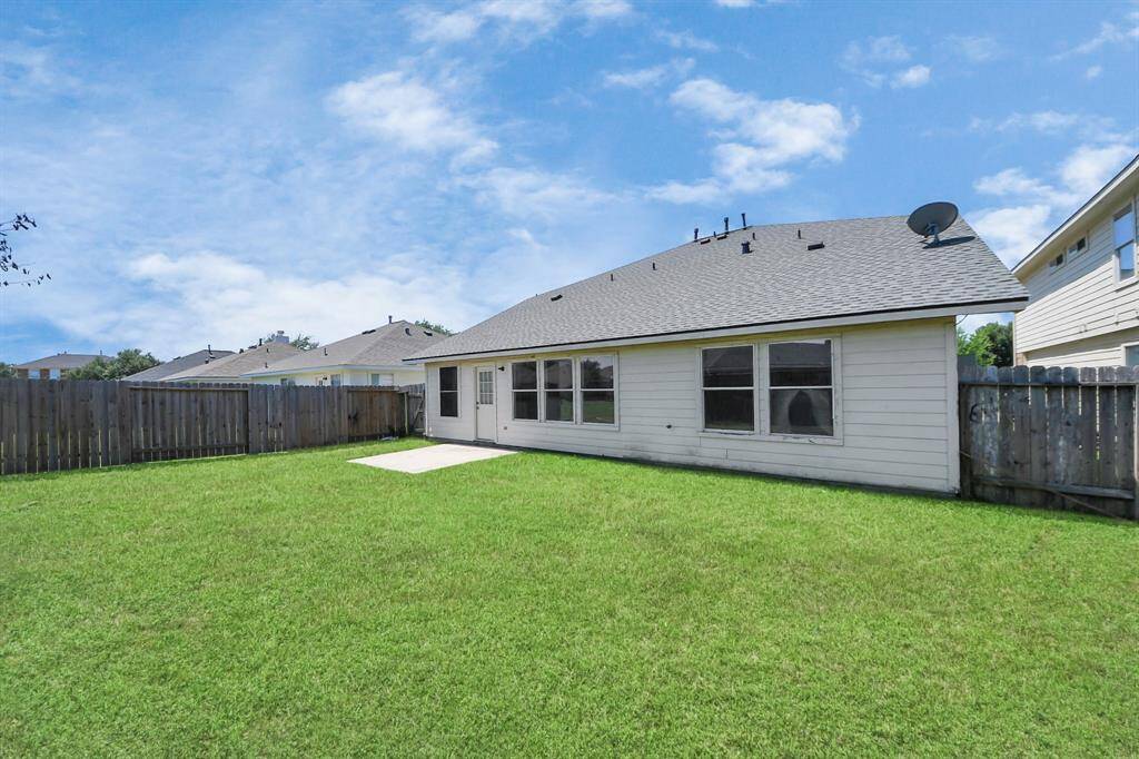 Spacious backyard with a well-maintained lawn, fenced for privacy, featuring a single-story house with large windows and a small patio area. Ideal for outdoor activities and relaxation.
