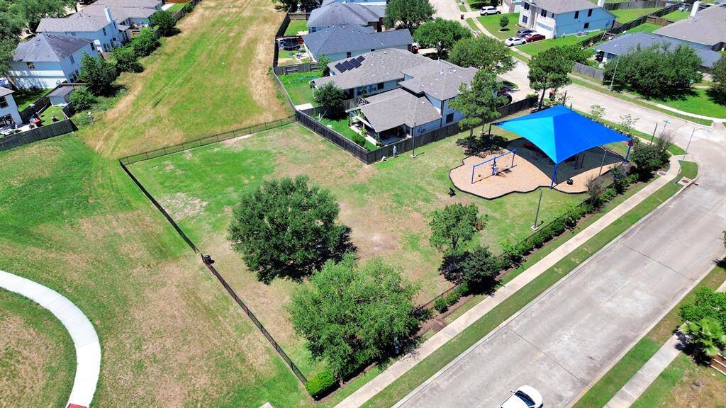 This aerial photo showcases a suburban neighborhood with a playground covered by a blue shade canopy. The area is surrounded by well-maintained homes and green spaces, offering a family-friendly environment with recreational amenities nearby.