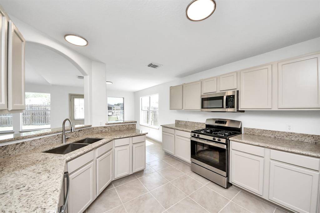 This kitchen features modern stainless steel appliances, ample cabinetry, granite countertops, and tile flooring. The open layout and large windows provide plenty of natural light, creating a bright and welcoming space.