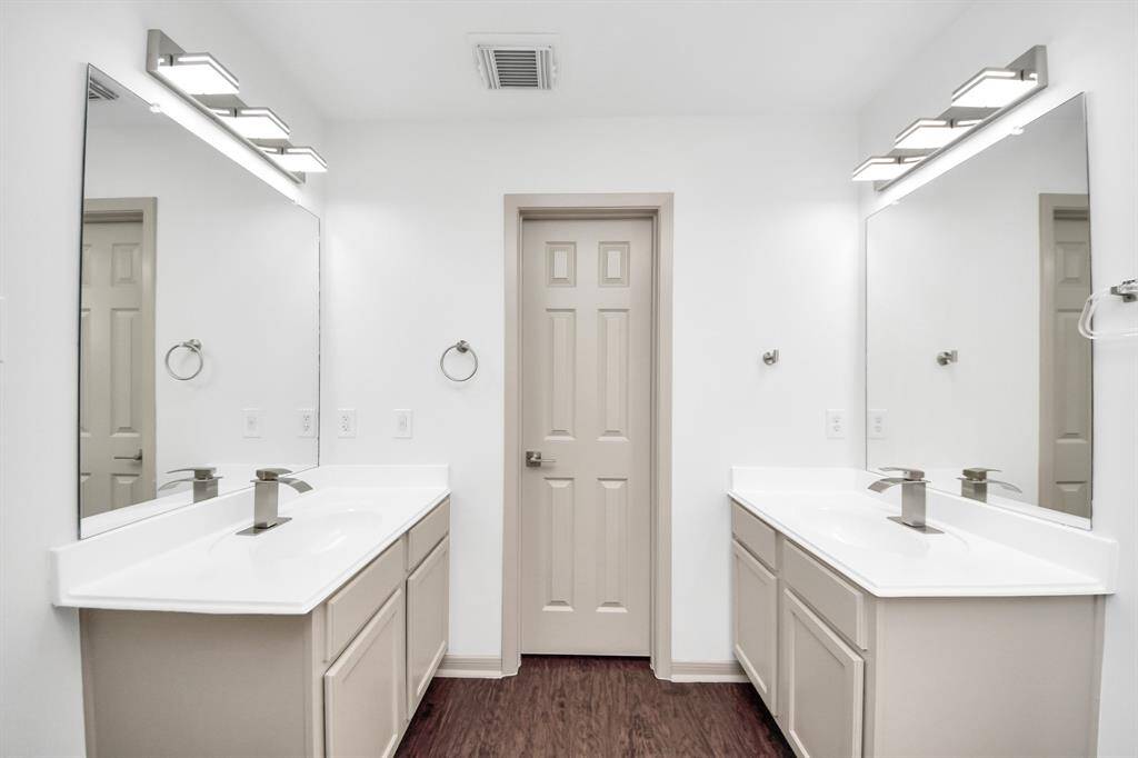 Modern bathroom with dual sinks, large mirrors, and sleek lighting. Features white cabinetry and countertops with a neutral color palette.